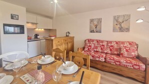 A dining area with a wooden table set for four, a sofa with a patterned cover, and artwork on the walls.