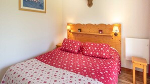 A bedroom with a wooden headboard, two bedside lamps, a bed with red floral bedding, a mounted deer head, and a framed picture on the wall. - Terrace Apartment in Chamrousse (Chamrousse)