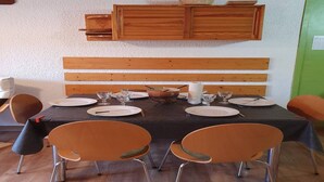 A dining area with a wooden bench, a table set with plates, glasses, and cutlery, and orange chairs.
