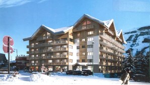 A multi-story hotel with balconies, a ski resort backdrop, and a snow-covered ground.