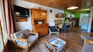 A cozy living room with wooden furniture, a flat-screen TV, and a dining area with a table and chairs.