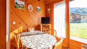 A wooden cabin interior with a dining table, chairs, a television, and artwork on the walls. - Chalet in Morillon near Ski Resort (Morillon)