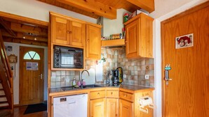 A compact kitchen with wooden cabinets, a microwave, a coffee maker, and a refrigerator. - Chalet in Morillon near Ski Resort (Morillon)