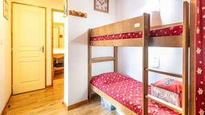 A bunk bed with a red floral bedspread, a wooden door, and a small framed picture on the wall. - Alpine Apartment with Terrace (Chamrousse)