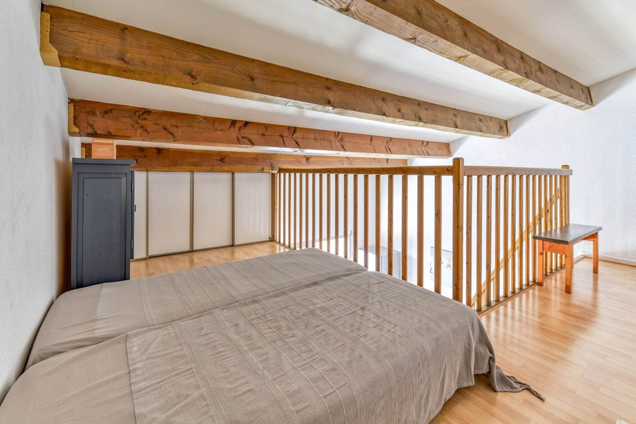 A bedroom with a bed, wooden ceiling beams, a small table, and a wardrobe.