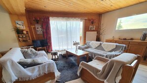 Ein gemütliches Wohnzimmer mit Holzmöbeln, einem Fernseher und einem großen Fenster mit Blick.