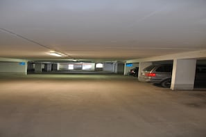 Garagem de estacionamento com piso de concreto e paredes brancas, com várias vagas e alguns carros estacionados.