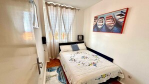 Quarto com uma cama, janela com cortinas, um quadro na parede e uma porta.