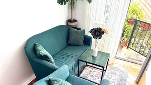 Um conjunto de sofá e poltrona cor azul-esverdeada, com almofadas combinando, uma mesa pequena com um vaso de flores e uma planta em vaso.