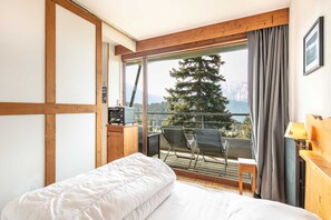 A bedroom with a large window, a bed, a TV, and a balcony with chairs. - Fully Equipped Stay, Chamrousse (Chamrousse)