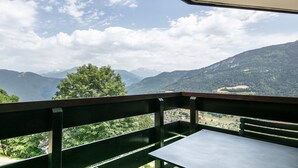 A balcony with a table and chairs, overlooking a mountainous landscape with a village below.