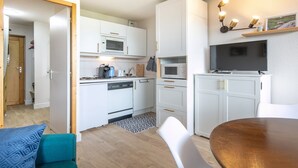 A modern kitchen with white cabinets, a microwave, a dishwasher, and a dining area with a wooden table and chairs.
