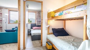 A room with a bunk bed, a sofa, and a desk. There is a window with a view of the mountains.