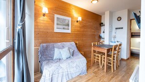 Une pièce chaleureuse avec un mur en bois, un canapé, une table à manger avec des chaises et un petit coin cuisine.