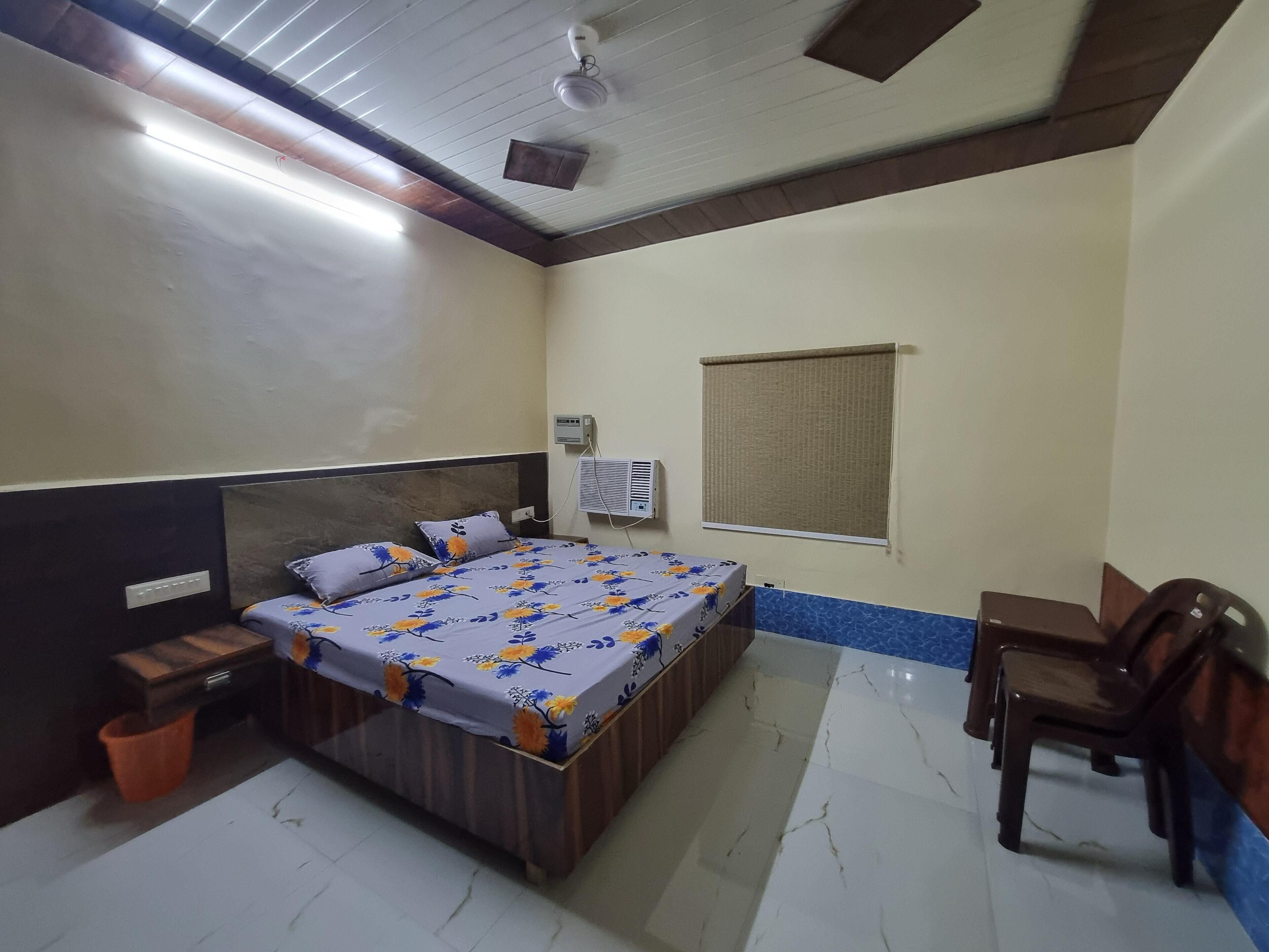 A bedroom with a bed, bedside table, chair, and an air conditioning unit.