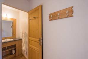 A wooden door with a handle and a white towel rack with three hooks on the wall.