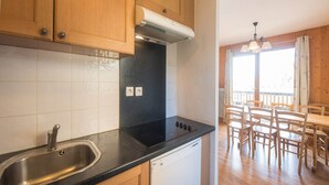 Une cuisine dotée d’un plan de travail noir, d’un évier en acier inoxydable et de meubles en bois. Elle comprend un lave-vaisselle et un coin repas avec une table et des chaises.