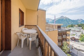 A balcony with a table and chairs, overlooking a mountainous landscape.