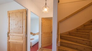Un escalier en bois mène à une chambre à coucher où se trouvent un lit et un luminaire suspendu.