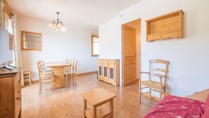 Une pièce spacieuse avec une table à manger en bois, des chaises, un petit banc en bois et un lit recouvert d’une couverture rouge.