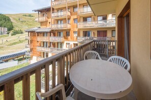A balcony with a round table and chairs, overlooking a mountainous area with a train track.