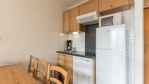 Una cocina compacta con armarios de madera, un refrigerador blanco, un microondas y una cafetera.