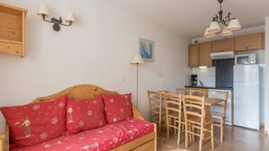 Una habitación acogedora con un sofá de madera, una mesa de comedor con sillas, una zona de cocina con armarios y electrodomésticos, y una lámpara de pared.