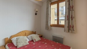 Un dormitorio con cama de madera, una mesita de noche, una lámpara de pared y un ventanal con cortinas.