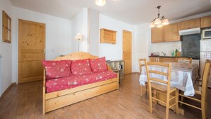 A cozy room with a wooden sofa, a dining table with chairs, and a kitchen area with wooden cabinets and appliances. - Apartment in Orcières with Heated Pool (Orcières)