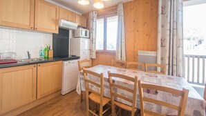 A kitchen with wooden cabinets, a microwave, a dishwasher, and a dining table with chairs. - Apartment in Orcières with Heated Pool (Orcières)