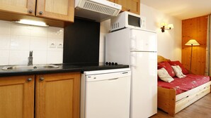 A compact kitchen with wooden cabinets, a built-in microwave, a white refrigerator, and a sink.