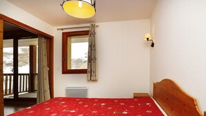A bedroom with a wooden bed, a window with curtains, a wall-mounted lamp, and a view of a snowy landscape.