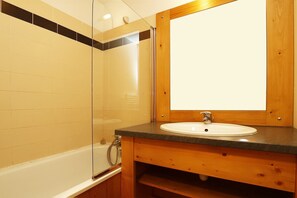 Un baño con bañera, tocador de madera con lavamanos y un espejo grande.