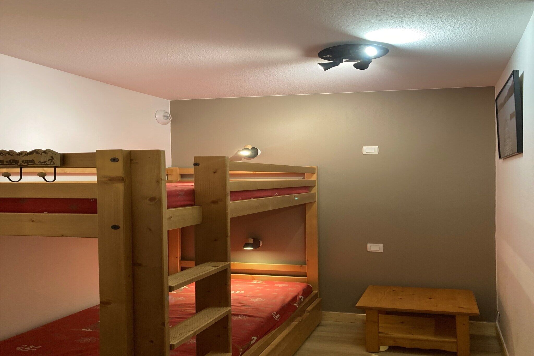 Une chambre avec un lit superposé, une petite table en bois et un luminaire fixé au plafond.
