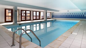 Une piscine intérieure avec des parois en verre transparent, un sol carrelé et un mur recouvert de carreaux bleus.