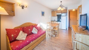 Ein gemütliches Zimmer mit einer Holzecke, einem Esstisch mit Stühlen, einer Küchenzeile mit Schränken und Geräten sowie einem Holzschrank mit Fernseher.