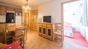Eine kompakte Küche mit Holzausstattung, einer Mikrowelle und einem Kühlschrank. Ein Esstisch mit Stühlen und ein kleiner Fernseher auf einer Holzkommode.