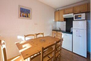 A small kitchen with wooden cabinets, a microwave, a dishwasher, and a dining table with chairs.