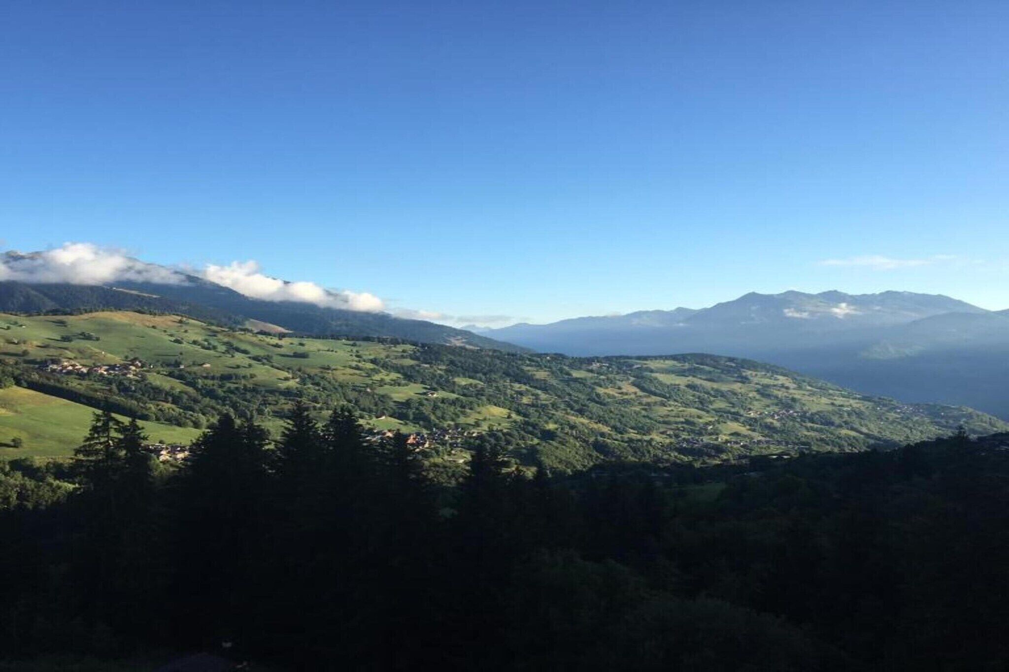 Vista panorámica de un paisaje montañoso con colinas ondulantes y edificios dispersos.