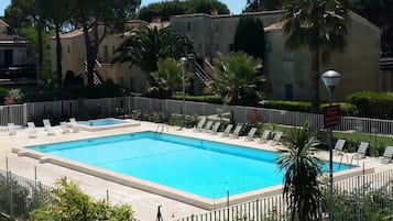 A rectangular swimming pool surrounded by a white fence, with lounge chairs and palm trees.