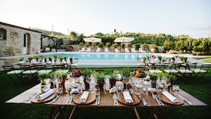 An outdoor dining area with tables set for a meal, overlooking a pool and garden.