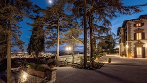A nighttime view of a building with a paved courtyard, surrounded by trees and a distant cityscape.