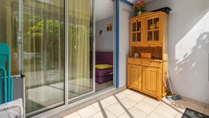 Et værelse med en skydedør af glas, der fører til en balkon, et træskab med glaslåger, en fejebakke og en lille lilla sofa.