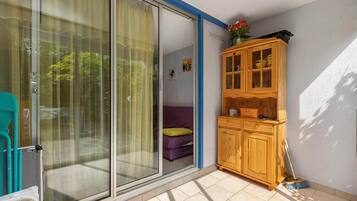 Ein Zimmer mit einer Schiebetür zum Balkon, einem Holzschrank mit Glastüren, einem Besen und einem kleinen, violetten Sofa.