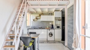 A compact kitchen with white cabinets, a washing machine, and a dining area with a table and chairs. - Modern Stay by the Beach (Agde)