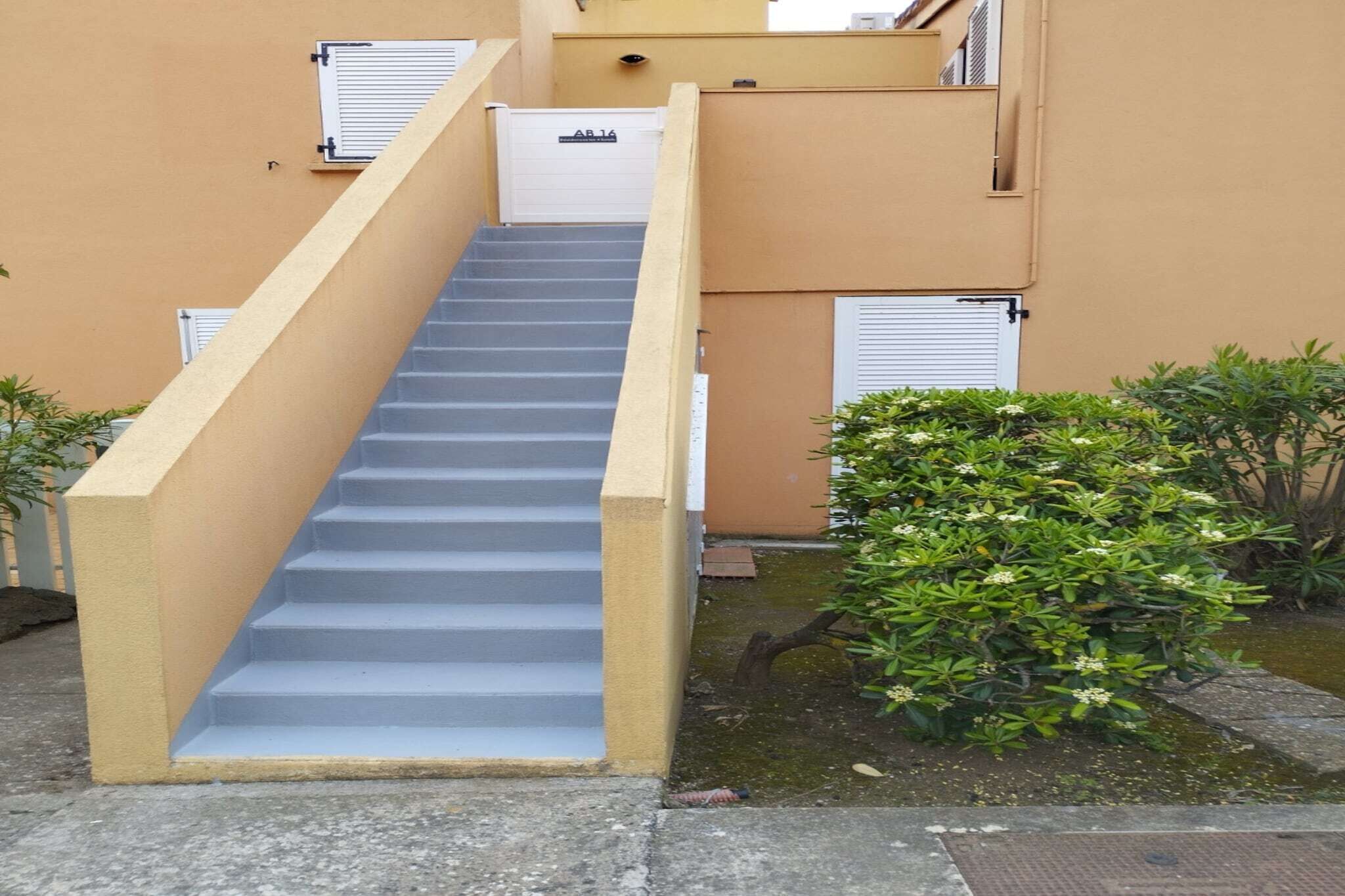 Una serie di gradini in cemento che conducono a un edificio con pareti beige e persiane bianche.