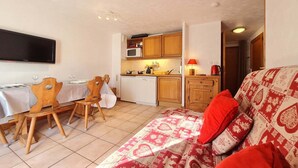 Ett kompakt bostadsutrymme med en matplats, ett litet kök och en soffa med mönstrat sänglinne.