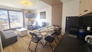 Een moderne woonkamer met een eethoek, een keuken met fornuis, en een groot raam met uitzicht op de stad.