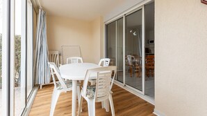 A balcony with a white table and chairs, a sliding glass door, and a view of the outside. - Charming Coastal Escape in Agde (Agde)