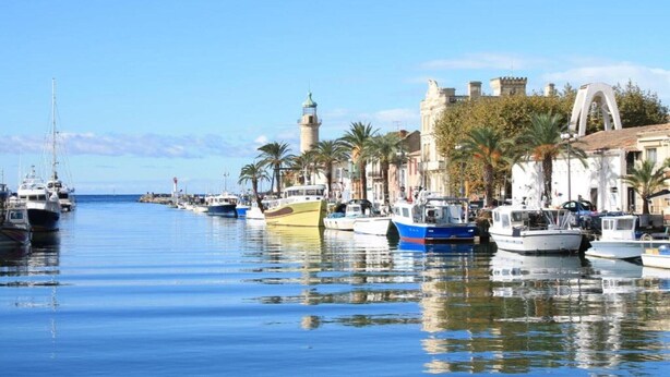 A marina with boats docked along a waterfront, a prominent lighthouse, and historic buildings with arches. - Modern Seaside Apartment (Le Grau-du-Roi)
